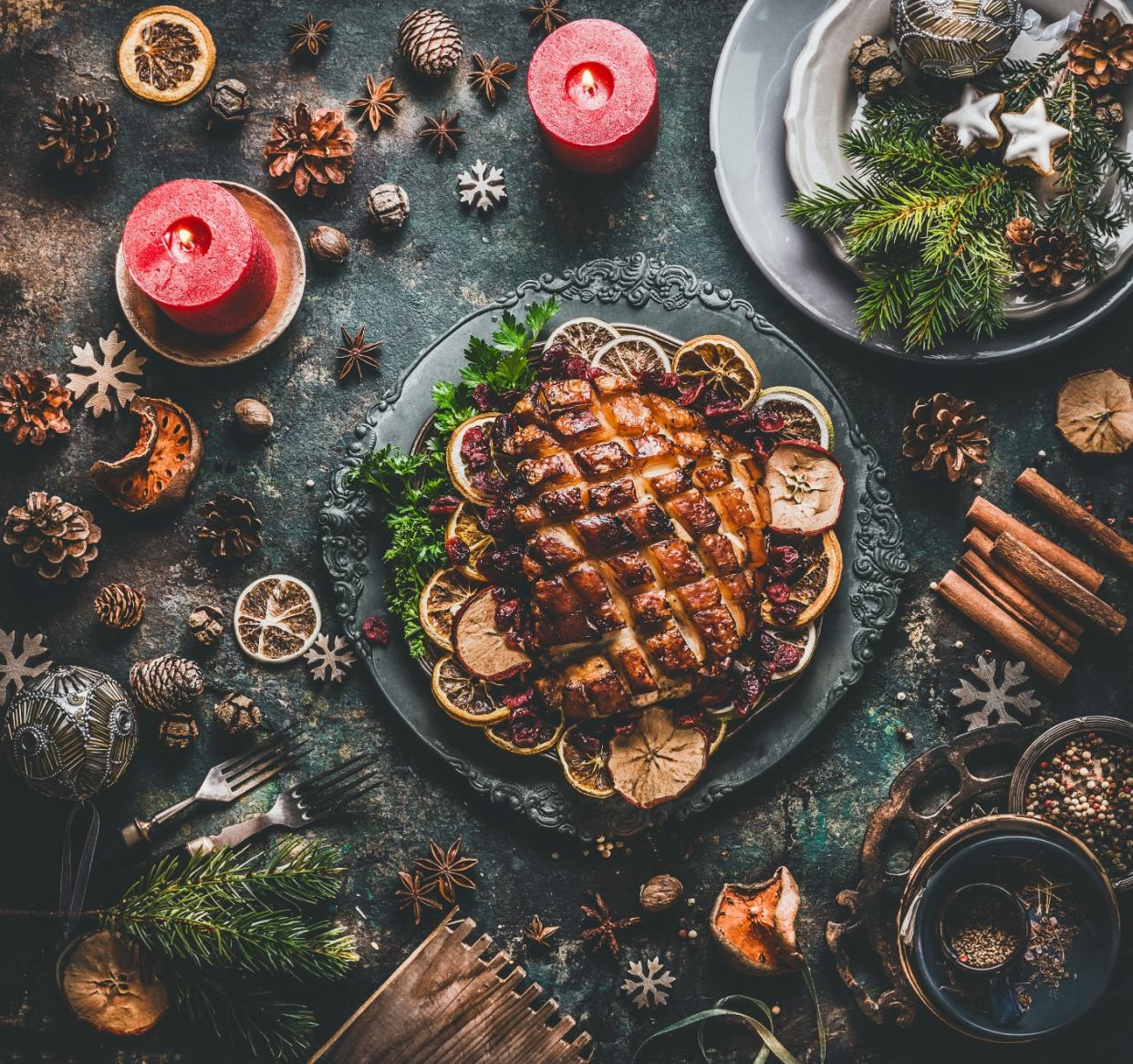 A top view of roasted turkey served on top of dried lemon and garnishing with pine cones, red candles and dried spices as Christmas decorations on a table.