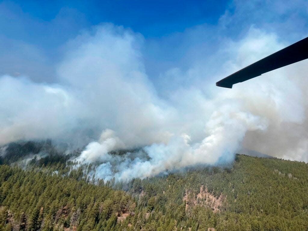 In this photo provided by the New Mexico National Guard, a New Mexico National Guard Aviation UH-60 Black Hawk flies as part of firefighting efforts, dropping thousands of gallons of water with Bambi buckets from the air on the Calf Canyon/Hermits Peak fire in northern New Mexico on Sunday, May, 1, 2022. Thousands of firefighters are battling destructive wildfires in the Southwest as more residents are preparing to evacuate.