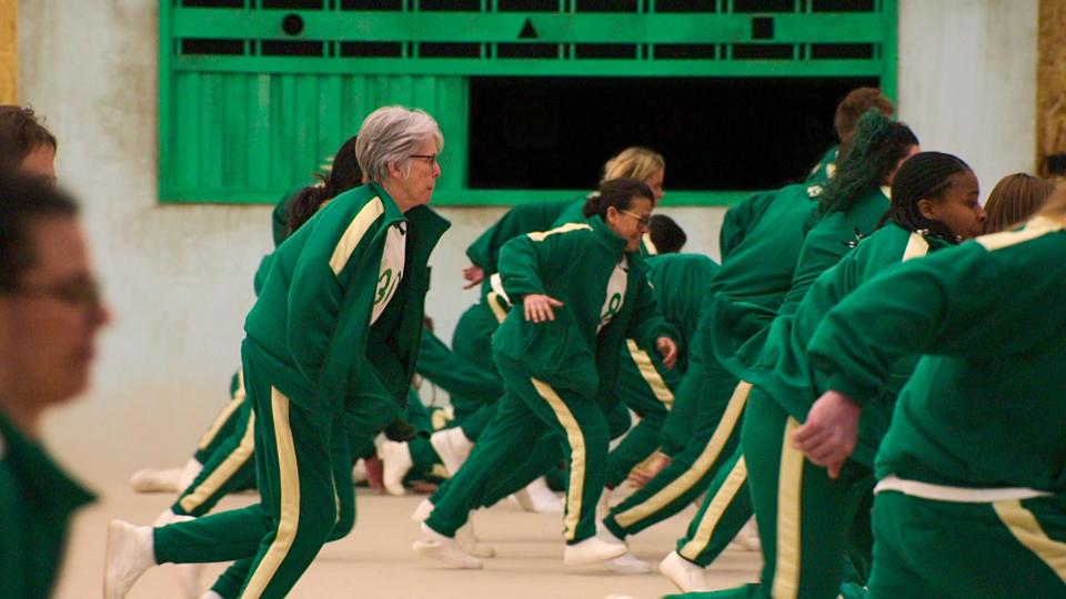 squid game players running while playing red light green light, all wearing green track suits