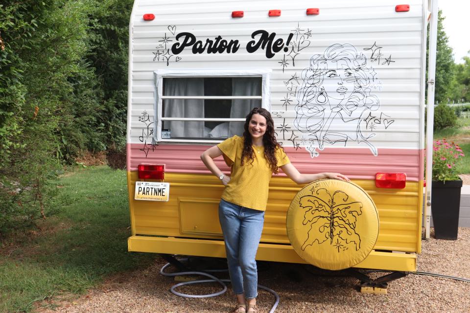 Reporter Talia Lakritz, wearing a yellow shirt and jeans, stands in front of a Dolly Parton-themed RV that says "Parton Me!" on the back.