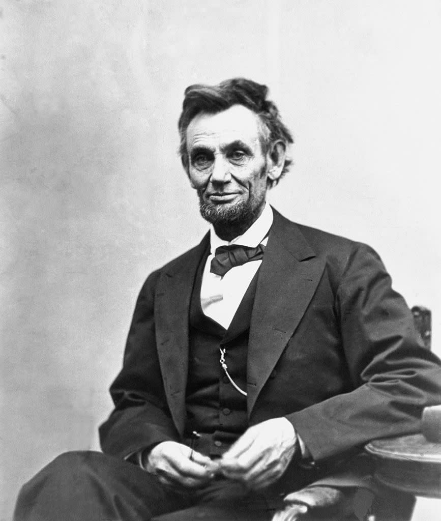 Abraham Lincoln seated, wearing a suit and bow tie, with his hands resting in his lap. 