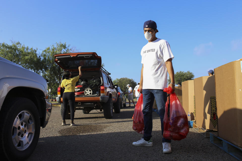 Roberto Palomo grabs a bag of food for one of the vehicles waiting in line Friday, July 10, 2020, for United Way of Southern Cameron County's food distribution event for residents affected by COVID-19 at Besteiro Elementary School in Brownsville, Texas.(Denise Cathey/The Brownsville Herald via AP)