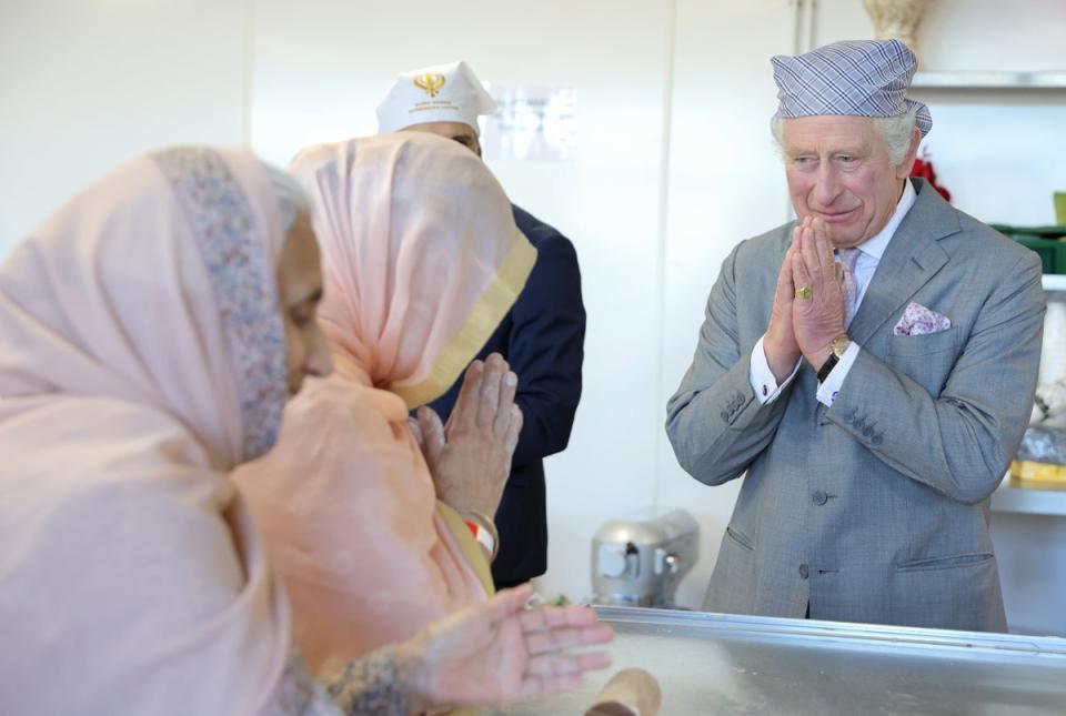 King Charles III makes the traditional namaste gesture as he speaks to volunteers and learns about the programmes they deliver for the local community (Getty Images)