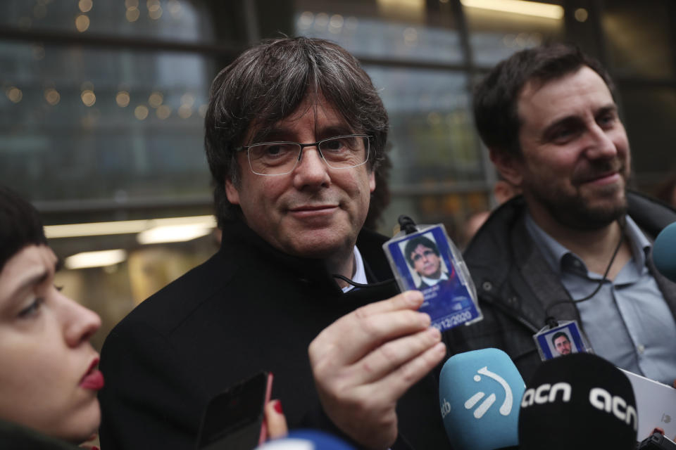 Catalonia's former regional president Carles Puigdemont, center, shows his accreditation badge as he stands next to former Catalan regional minister Antoni Comin outside the European Parliament in Brussels, Friday, Dec. 20, 2019. In a potentially stinging reversal for Spanish justice authorities, the European Union's top court ruled that a former Catalan official serving a prison sentence for his role in a banned independence referendum two years ago had the right to parliamentary immunity when he was on trial. (AP Photo/Francisco Seco)