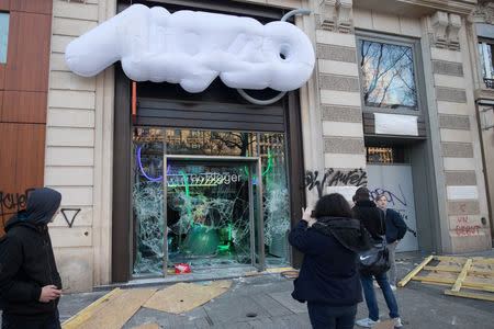 People take pictures of a damaged shop during a demonstration by the "yellow vests" movement on the Champs Elysees avenue in Paris, France, March 16, 2019. Picture taken March 16, 2019. REUTERS/Philippe Wojazer