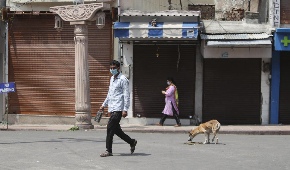 Indians wearing face masks as a precaution against the coronavirus walk past closed market during reimposed weekend lockdown to prevent the spread of new coronavirus in Jammu, India, Sunday, July 26, 2020. India is the third hardest-hit country by the pandemic in the world after the United States and Brazil. (AP Photo/Channi Anand)