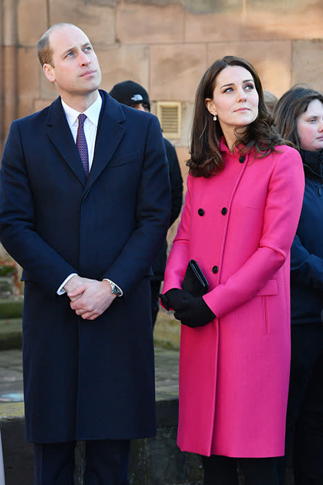 Prince William in a dark navy blue topcoat and Kate in a hot pink coat together looking up outside