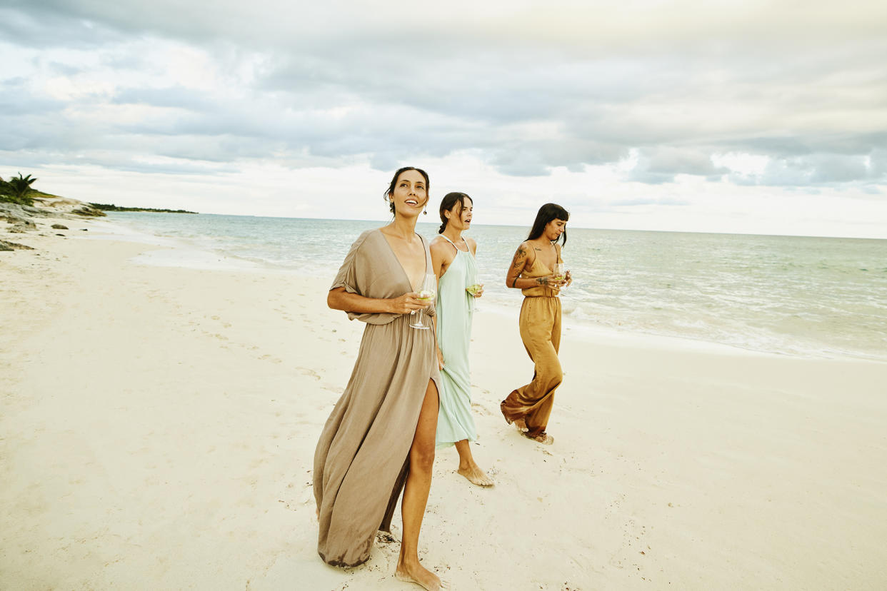 Wide shot of female friends walking on beach at tropical resort at sunset