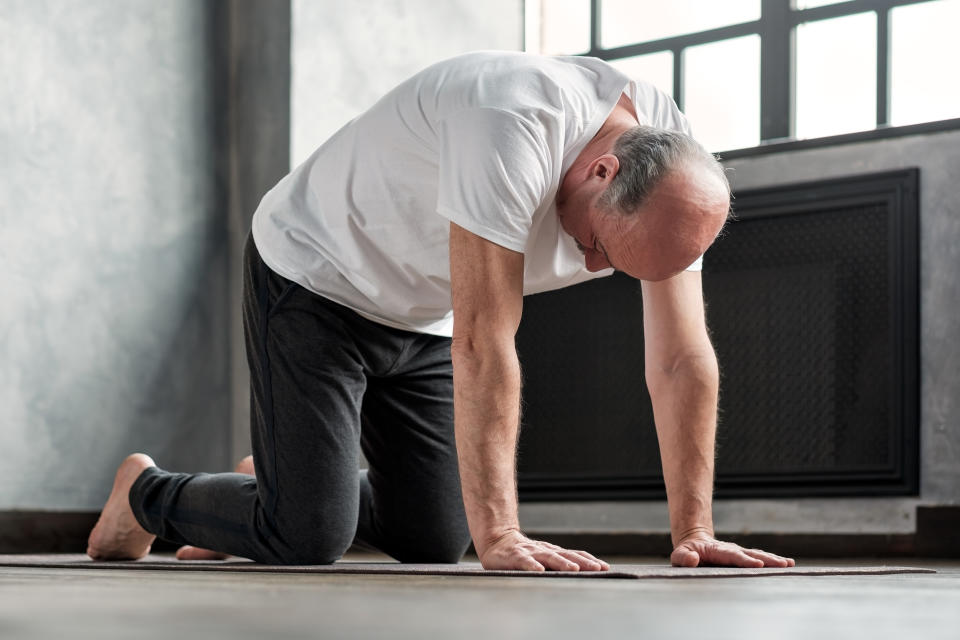 Senior bald yogi men practices yoga asana marjariasana or cat-cow pose at home�