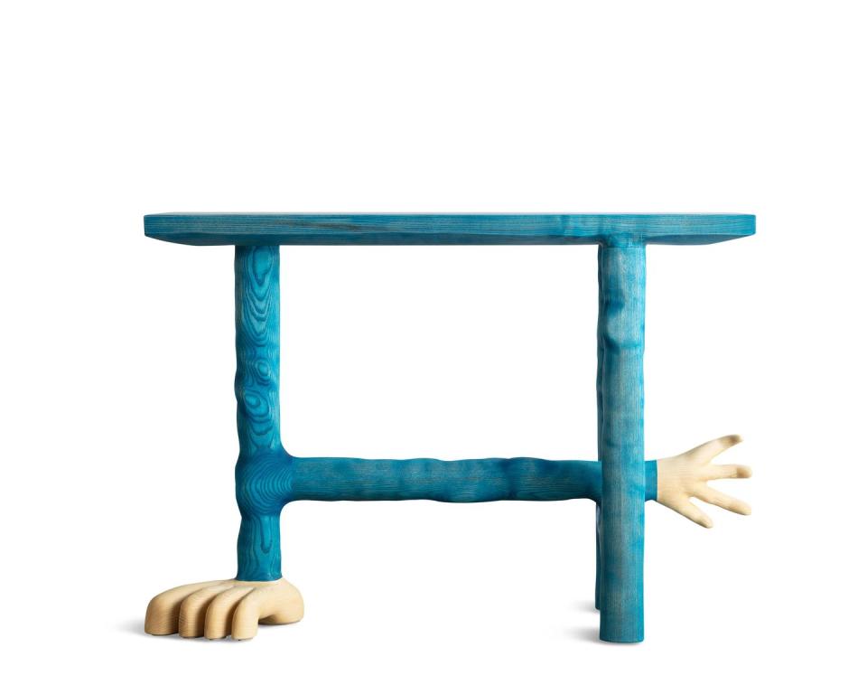 blue wood table with a hand finial on the end of the cross bar and a foot at the end of one of the legs