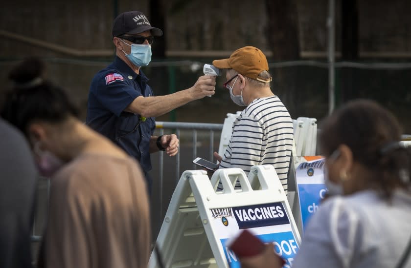 Anaheim, CA - January 13: An Anaheim firefighter takes the temperature of Orange County active Phase 1A (critical and healthcare workers) residents as they enter large tents at Orange County's first large-scale vaccination site to receive the Moderna COVID-19 vaccine in the Toy Story parking lot at the Disneyland Resort in Anaheim Wednesday, Jan. 13, 2021. Orange County supervisors and Orange County Health Care Agency Director Dr. Clayton Chau held a news conference discussing the county's first Super POD (point-of-dispensing) site for COVID-19 vaccine distribution. The vaccinations are at Tier 1A for people who have reservations on a website. The site is able to handle 7,000 immunizations per day. Their goal is to immunize everyone in Orange County who chooses to do so by July 4th. (Allen J. Schaben / Los Angeles Times)