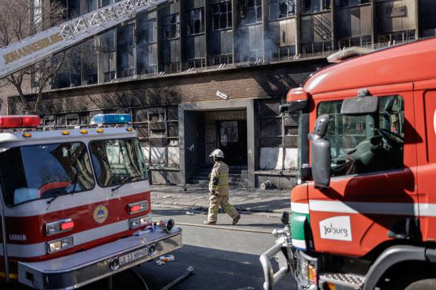 A South African firefighter walks past fire engines at the scene of a fire in Johannesburg on 31 August 2023 (AFP via Getty Images)