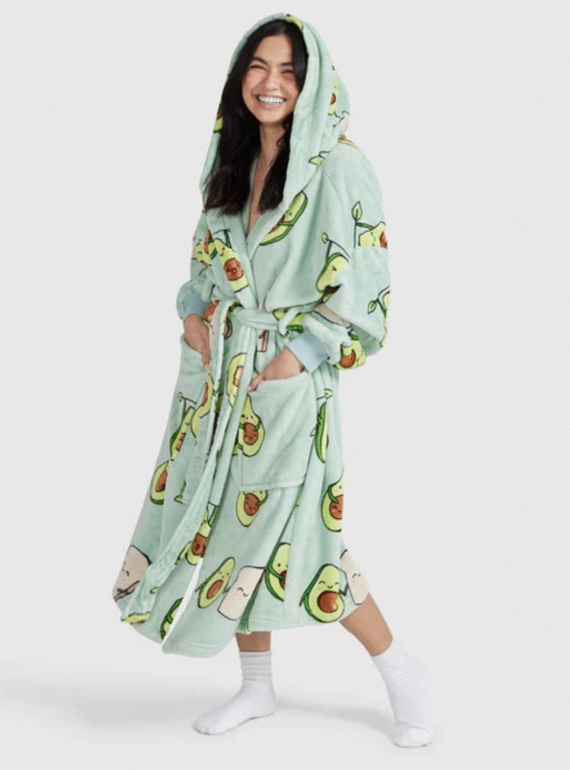 A young woman stands smiling in her avocado themed Oodie robe