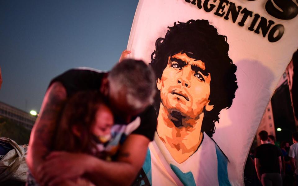 A father and her daughter, fans of Argentinian football legend Diego Maradona, mourn as they gather by the Obelisk to pay homage on the day of his death in Buenos Aires - AFP