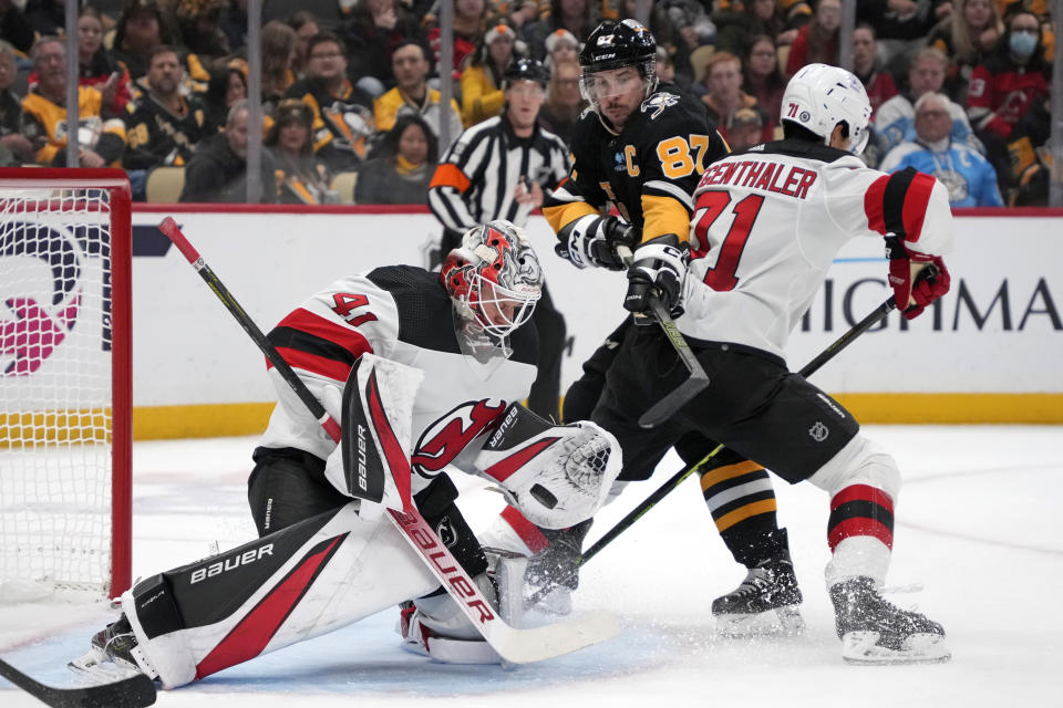 New Jersey Devils goaltender Vitek Vanecek (41) blocks a shot with Pittsburgh Penguins' Sidney Crosby (87) trying to get his stick on the puck with Devils' Jonas Siegenthaler, right, defending during the second period of an NHL hockey game in Pittsburgh, Thursday, Nov. 16, 2023. (AP Photo/Gene J. Puskar)