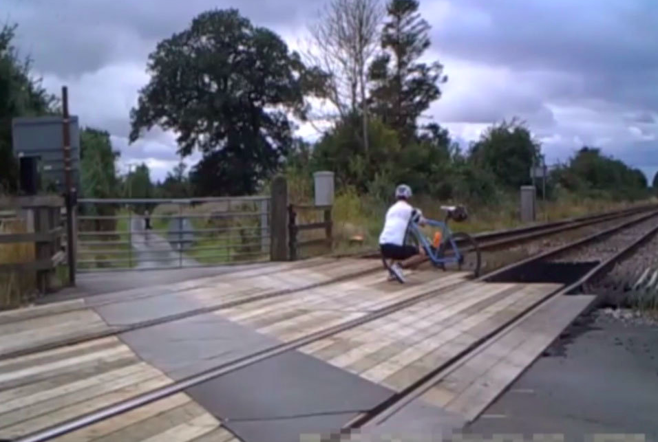 A cyclist is seen wedging his bike in the tracks to help a rider through the gate on to the crossing. (SWNS)