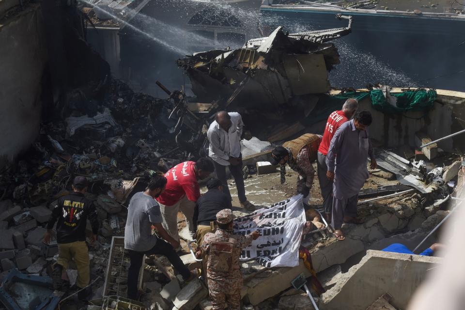 EDITORS NOTE: Graphic content / Rescue workers cover the body of a victim they recovered from the rubbles after a Pakistan International Airlines flight crashed in a residential neighbourhood in Karachi on May 22, 2020. - A Pakistan passenger plane with more than 100 people believed to be on board crashed in the southern city of Karachi on May 22, the country's aviation authority said. (Photo by Asif HASSAN / AFP) (Photo by ASIF HASSAN/AFP via Getty Images)