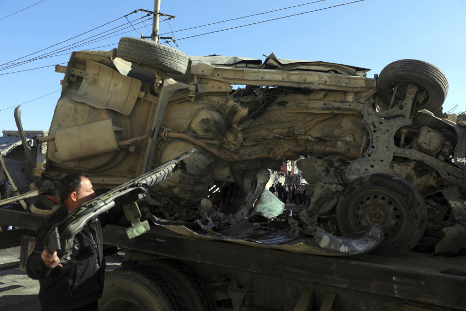 Afghan security watches the removal of a damaged vehicle after a roadside bomb attack in Kabul, Afghanistan, Tuesday, Dec. 22, 2020. A roadside bomb tore through a vehicle in the Afghan capital of Kabul Tuesday, killing multiple people, police said. (AP Photo/Rahmat Gul)