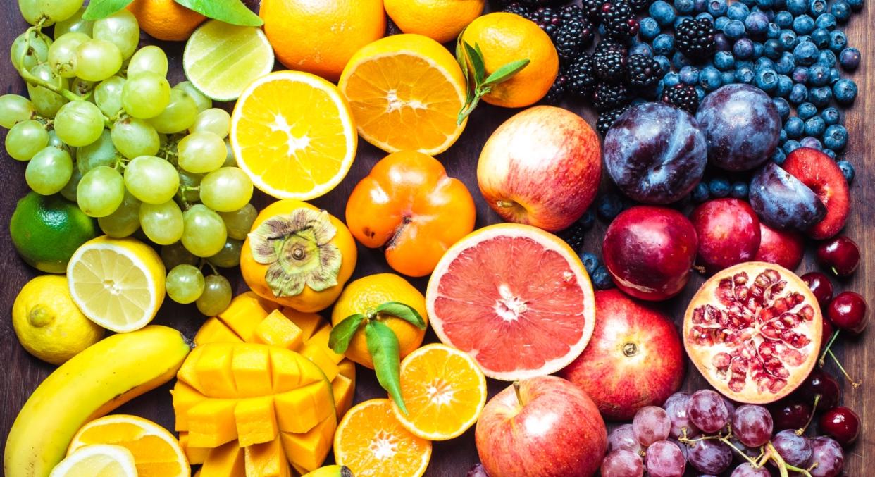 A colourful board filled with fruits, from grapes to lemons to oranges to bananas to mangoes to blueberries to apples to pomegranates