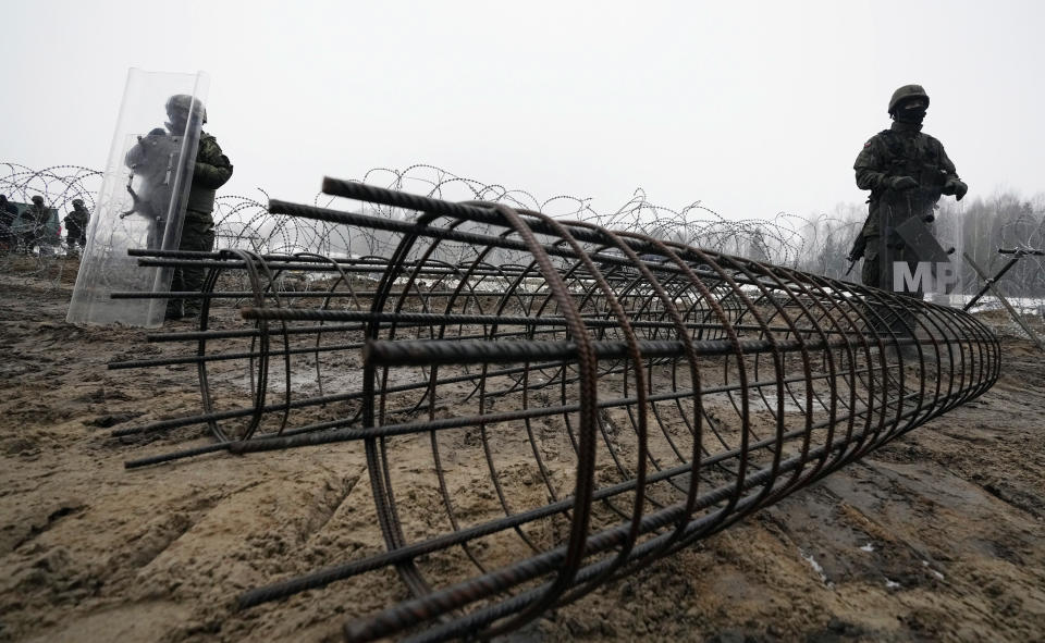 FILE-Guards and the military watching the start of work on the first part of a 180 kilometers (115 miles) and 5.5 meter (18ft)-high metal wall intended to block migrants from Belarus crossing illegally into EU territory, in Tolcze, near Kuznica, Poland, Jan. 27, 2022. A year after migrants started crossing into the European Union from Belarus to Poland, Polish authorities are planning to announce Thursday that a 5.5-meter-tall steel wall along its border to the north with Belarus is set to be completed. (AP Photo/Czarek Sokolowski, File)