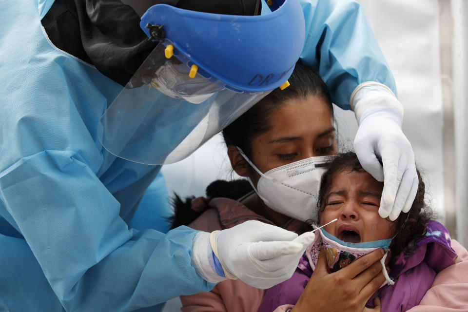 Dr. Victor Hugo Santamaria tests 2-year-old Regina Chavez for COVID-19 as she is held by her mother Edith Monserrat Bautista, in a tent set up to perform rapid coronavirus testing at the TAPO bus station in the Venustiano Carranza borough of Mexico City, Friday, Nov. 20, 2020. Mexico passed the 100,000 mark in confirmed COVID-19 deaths on Thursday, becoming only the fourth country to do so. (AP Photo/Rebecca Blackwell)