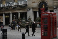 People wearing face masks walk and stand backdropped by Christmas trees in Covent Garden, during England's second coronavirus lockdown in London, Thursday, Nov. 26, 2020. As Christmas approaches, most people in England will continue to face tight restrictions on socializing and business after a nationwide lockdown ends next week, the government announced Thursday. (AP Photo/Matt Dunham)