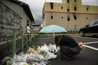 FILE - In this July 19, 2019, file photo, a woman prays at a makeshift memorial to honor the victims of a fire at the building of Kyoto Animation's No. 1 studio, background, in Kyoto, western Japan. Japanese police on Wednesday, May 27, 2020, arrested 42-year-old Shinji Aoba, the suspect in a deadly arson at the animation studio after the alleged attacker regained enough strength from his own injury to respond to police investigation. Aoba is accused of storming into the studio, setting it on fire and killing 36 people. (AP Photo/Jae C. Hong, File)