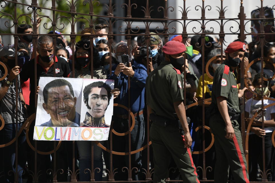 Government supporters, one with photos of late Venezuelan President Hugo Chavez, left, and independence hero Simon Bolivar with the Spanish message "We're back," stand outside the National Assembly where lawmakers are being sworn-in, in Caracas, Venezuela, Tuesday, Jan. 5, 2021. The ruling socialist party assumed the leadership of Venezuela's congress on Tuesday, the last institution in the country it didn't already control. (AP Photo/Matias Delacroix)