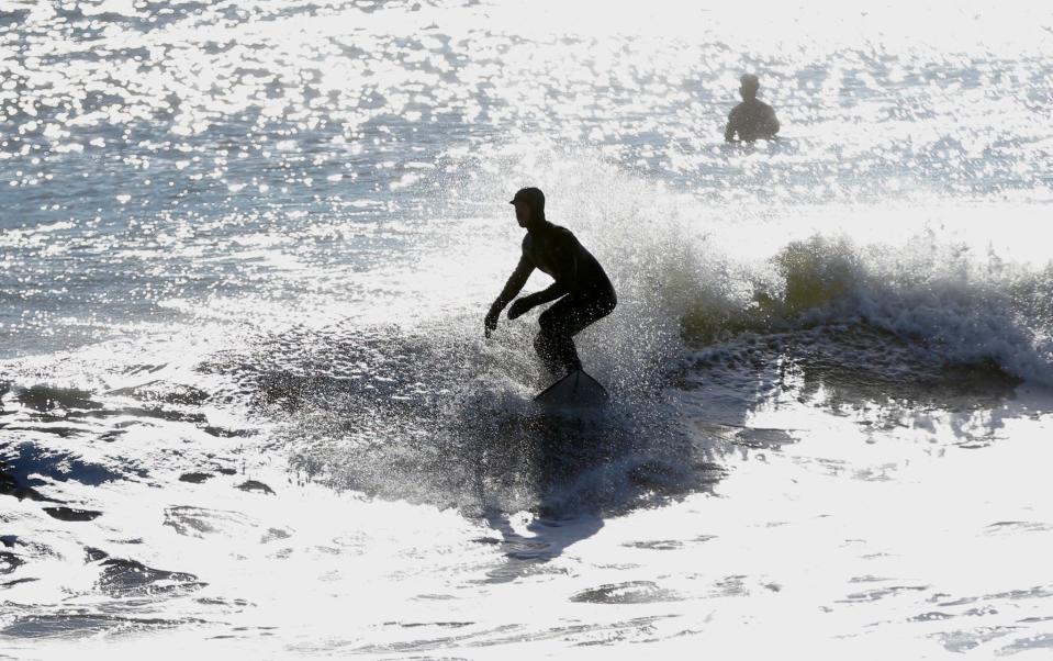 A surfer catches waves at North Hampton State Park Sunday, Jan. 30, 2022, a day after a blizzard hit the area.