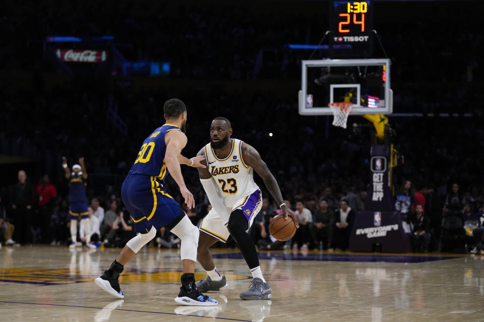 Los Angeles Lakers forward LeBron James (23) looks up at the shot clock over Golden State Warriors guard Stephen Curry (30) during the second half of an NBA basketball game in Los Angeles, Saturday, March 16, 2024. Play was delayed after a shot clock malfunction. (AP Photo/Ashley Landis)