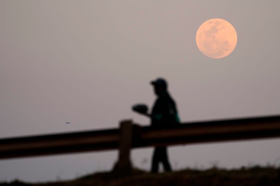 A Supermoon is seen on the sky as a woman walks on the street, in Vosloorus, east of Johannesburg, South Africa, Wednesday, Aug. 30, 2023. August 30 sees the month’s second supermoon, when a full moon appears a little bigger and brighter thanks to its slightly closer position to Earth. (AP Photo/Themba Hadebe)