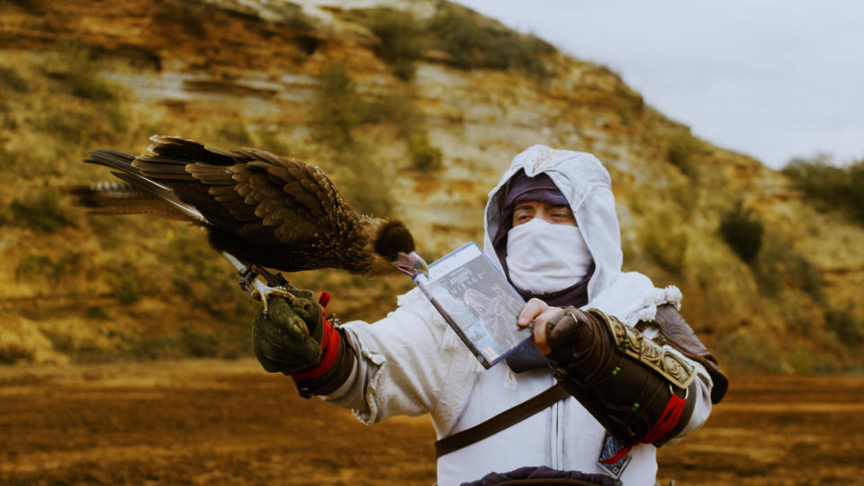 A man with a bird holding a copy of Assassin's Creed.