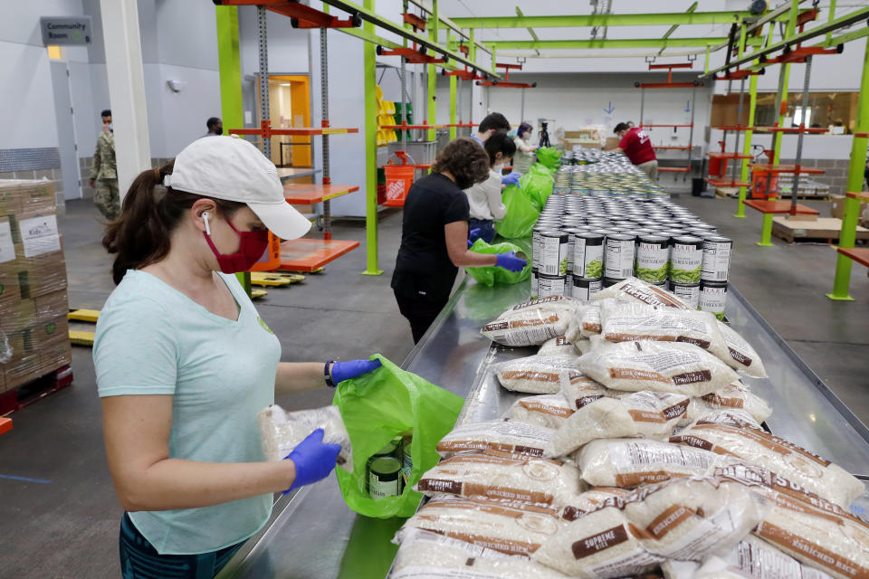 Volunteers load non perishable foods green grocery bag that are then boxed up and put on a pallet for distribution to a school student food program in the area at the Houston Food Bank Wednesday, Oct. 14, 2020, in Houston. (AP Photo/Michael Wyke)