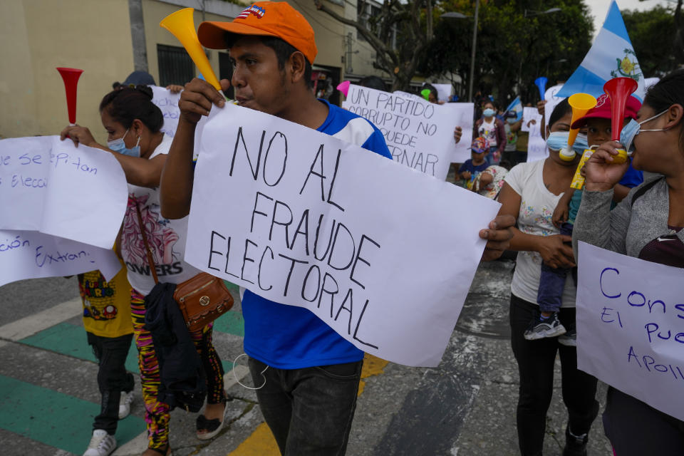 A protester blows on noise maker holding a poster with a message that reads in Spanish: "No to electoral fraud," during a protest alleging fraud in the runoff presidential election, in front of the Supreme Electoral Tribunal building, in Guatemala City, Wednesday, Aug. 30, 2023. The party of former first lady Sandra Torres, who lost to rival Bernardo Arevalo, filed a complaint Aug. 25th, alleging fraud in the way the votes were counted. (AP Photo/Moises Castillo)