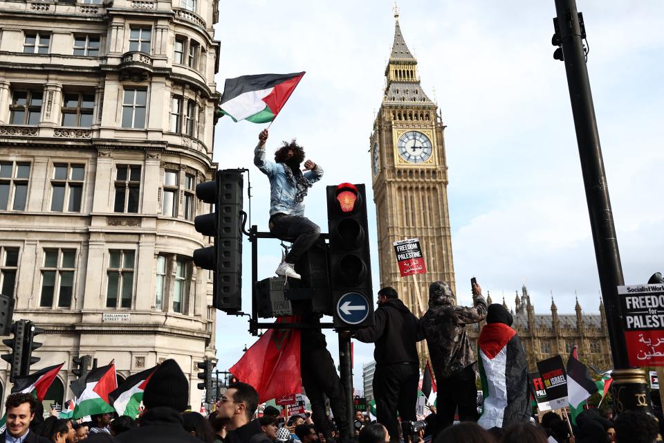 A protester waves a Palestinian flag while sitting on a set of traffic lights in Parliament Square after taking part in a 'March For Palestine' in London on October 28, 2023, to call for a ceasefire in the conflict between Israel and Hamas. Thousands of civilians, both Palestinians and Israelis, have died since October 7, 2023, after Palestinian Hamas militants based in the Gaza Strip entered southern Israel in an unprecedented attack triggering a war declared by Israel on Hamas with retaliatory bombings on Gaza. (Photo by HENRY NICHOLLS / AFP) (Photo by HENRY NICHOLLS/AFP via Getty Images)