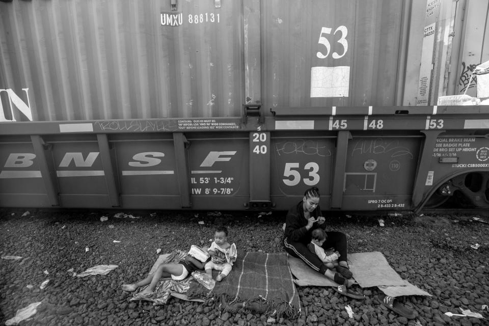 A family with infant children sits next to a train in Chihuahua City. The family, alone with other migrants waited to see if the train would head toward the border city of Ciudad Juárez.