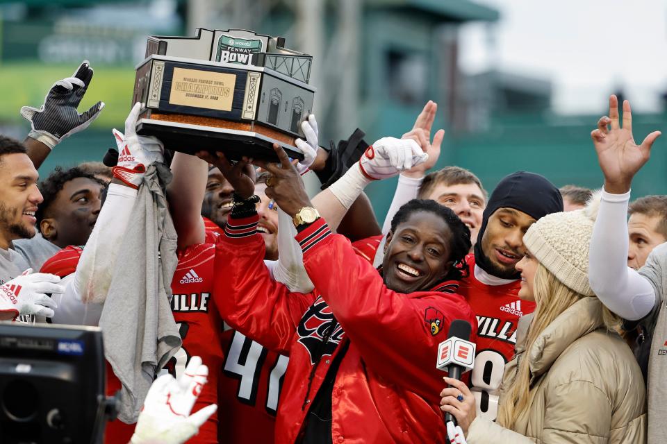 Louisville head coach Deion Branch holds up the trophy as his players celebrate around him after their 24-7 win over Cincinnati in the Fenway Bowl NCAA college football game at Fenway Park Saturday, Dec. 17, 2022, in Boston. (AP Photo/Winslow Townson)