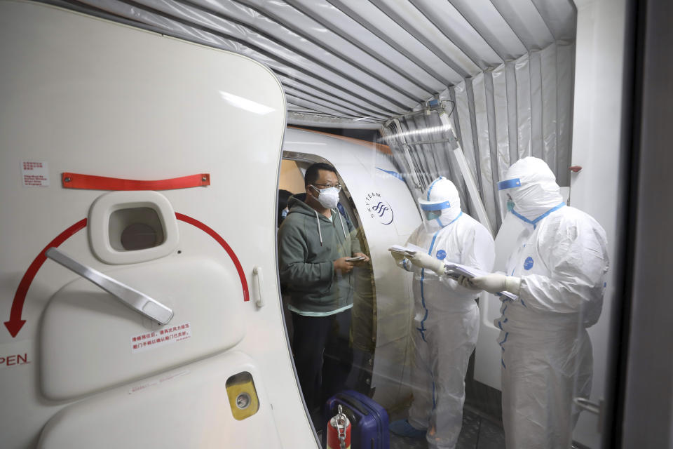 Quarantine workers in protective suits check identity documents as tourists from the Wuhan area walk off of a chartered plane taking them home from Bangkok at Wuhan Tianhe International Airport in Wuhan in central China's Hubei Province, Friday, Jan. 31, 2020. A group of Chinese tourists who have been trapped in Thailand since Wuhan was locked down due to an outbreak of new virus returned to China on Friday. (Chinatopix via AP)