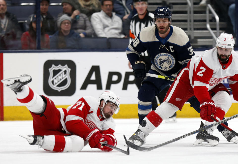 Detroit Red Wings forward Dylan Larkin, left, reaches for the puck in front of Columbus Blue Jackets forward Boone Jenner, center, and Red Wings defenseman Nick Leddy during the first period of an NHL hockey game in Columbus, Ohio, Monday, Nov. 15, 2021. (AP Photo/Paul Vernon)