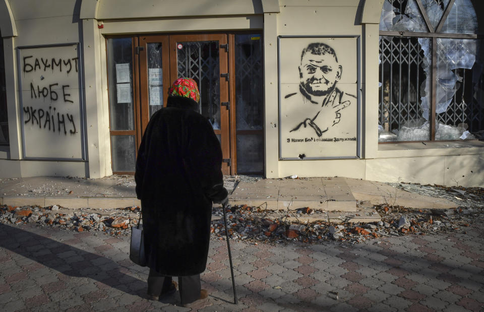 An elderly woman looks at a graffiti depicting General Valery Zaluzhny, head of Ukraine's armed forces and writing "God is with us and commander Zaluzhny" in the site of the heaviest battles with the Russian invaders in Bakhmut, Ukraine, Tuesday, Dec. 20, 2022. (AP Photo/Andriy Andriyenko)