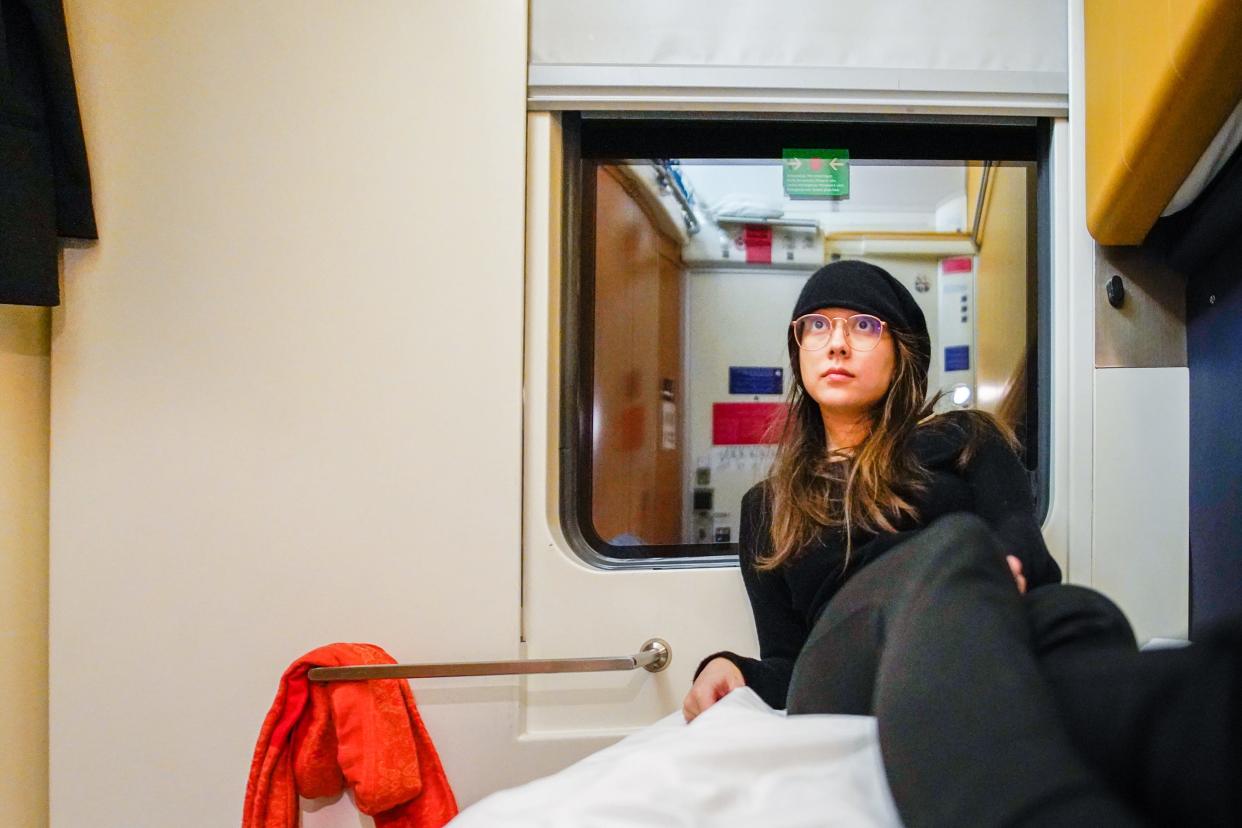 The author sits on a white bunk inside an overnight train cabin with a dark window behind her.