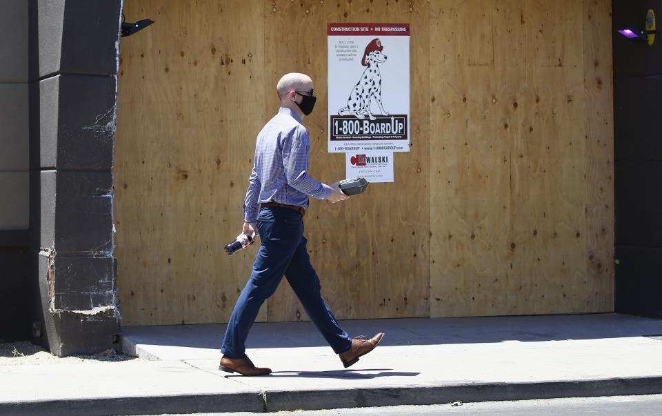 A pedestrian with a takeout lunch in hand walks through an area of Scottsdale, Ariz., known for busy restaurants, bars and nightlife Tuesday, June 30, 2020, with most businesses closed for the next 30 days due to the surge in coronavirus cases in Arizona. (AP Photo/Ross D. Franklin)