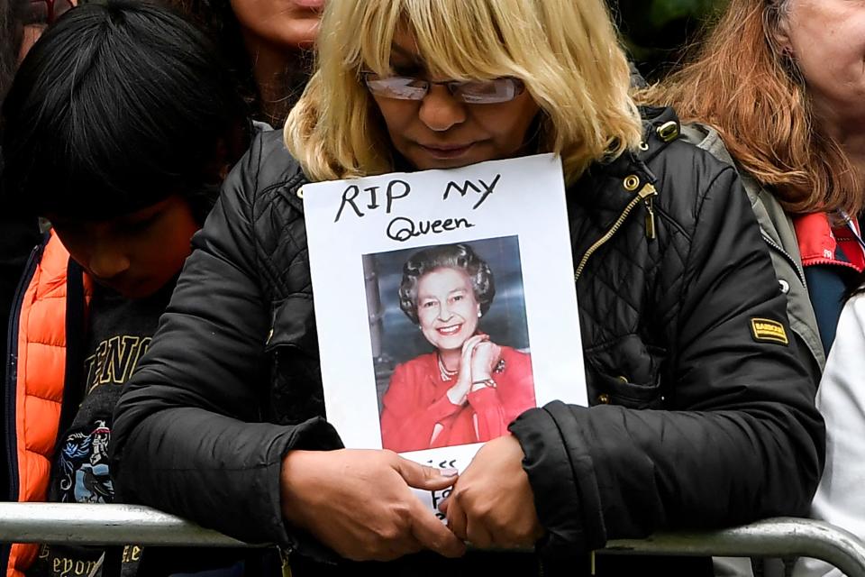 A mourner holds a photo of Queen Elizabeth II that is inscribed "RIP my Queen."