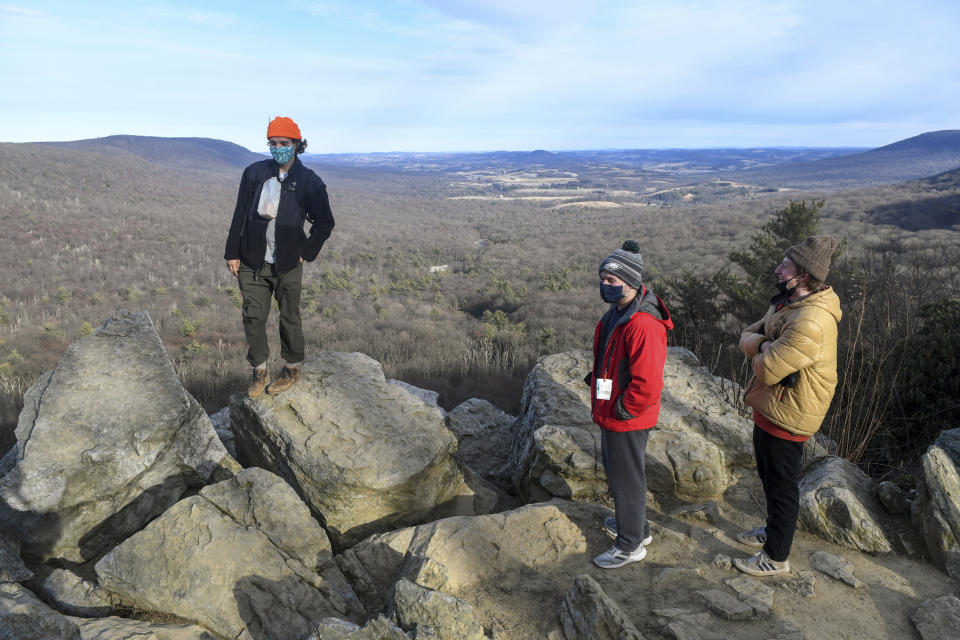 Keilan Barber, of West Chester, Pa., left, Christian Martella, center, and Ben Savitz, both of Havertown, Pa., hang out on the rocks at the South Lookout after hiking at Hawk Mountain Sanctuary in Kempton, Pa., in this Sunday, Jan. 24, 2021, file photo. During the pandemic, people around the world sought relief from lock downs and working from home in leisure sports.(Jacqueline Dormer/Republican-Herald via AP, File)