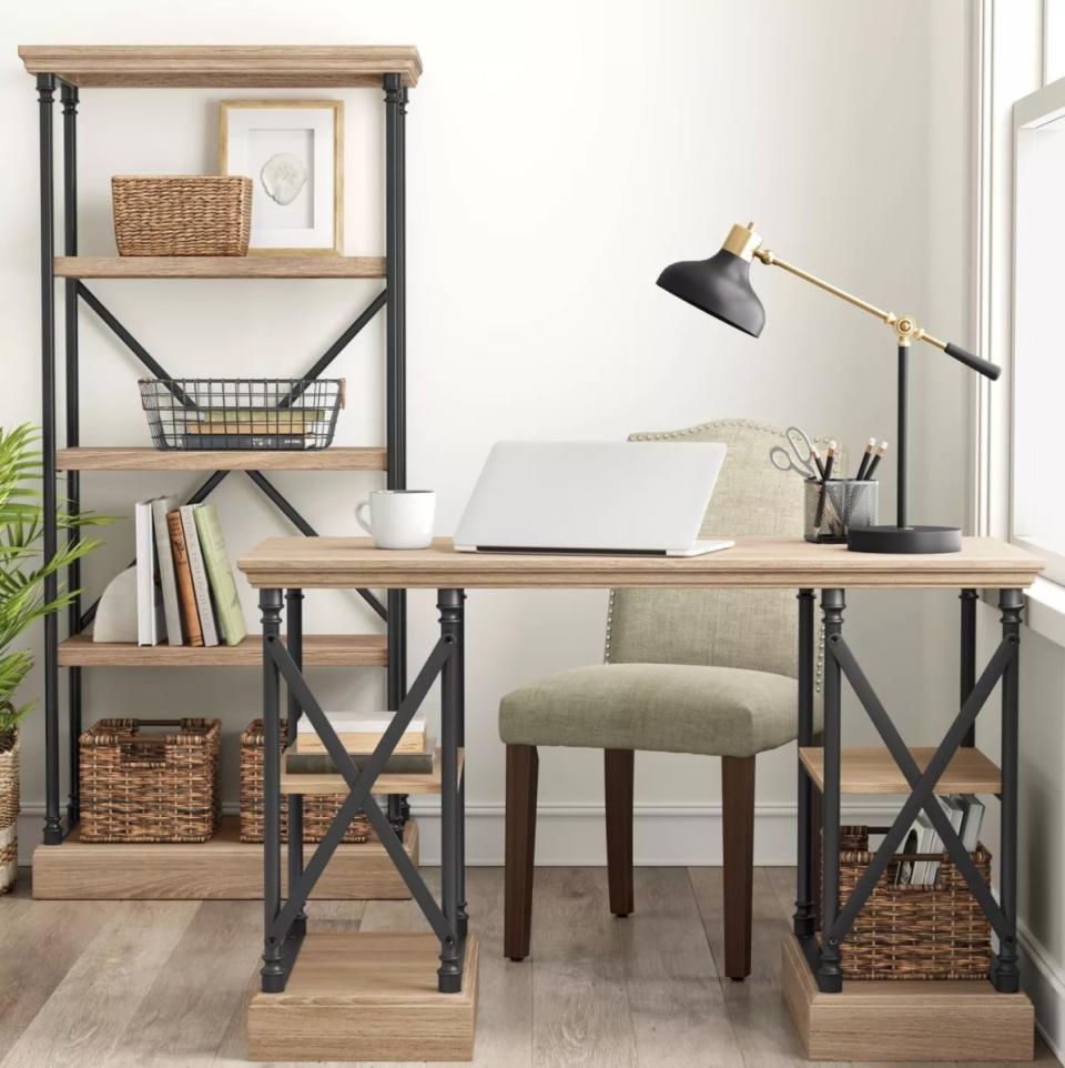 The cast iron bookshelf in light brown holding books, wicker baskets, and a framed drawing