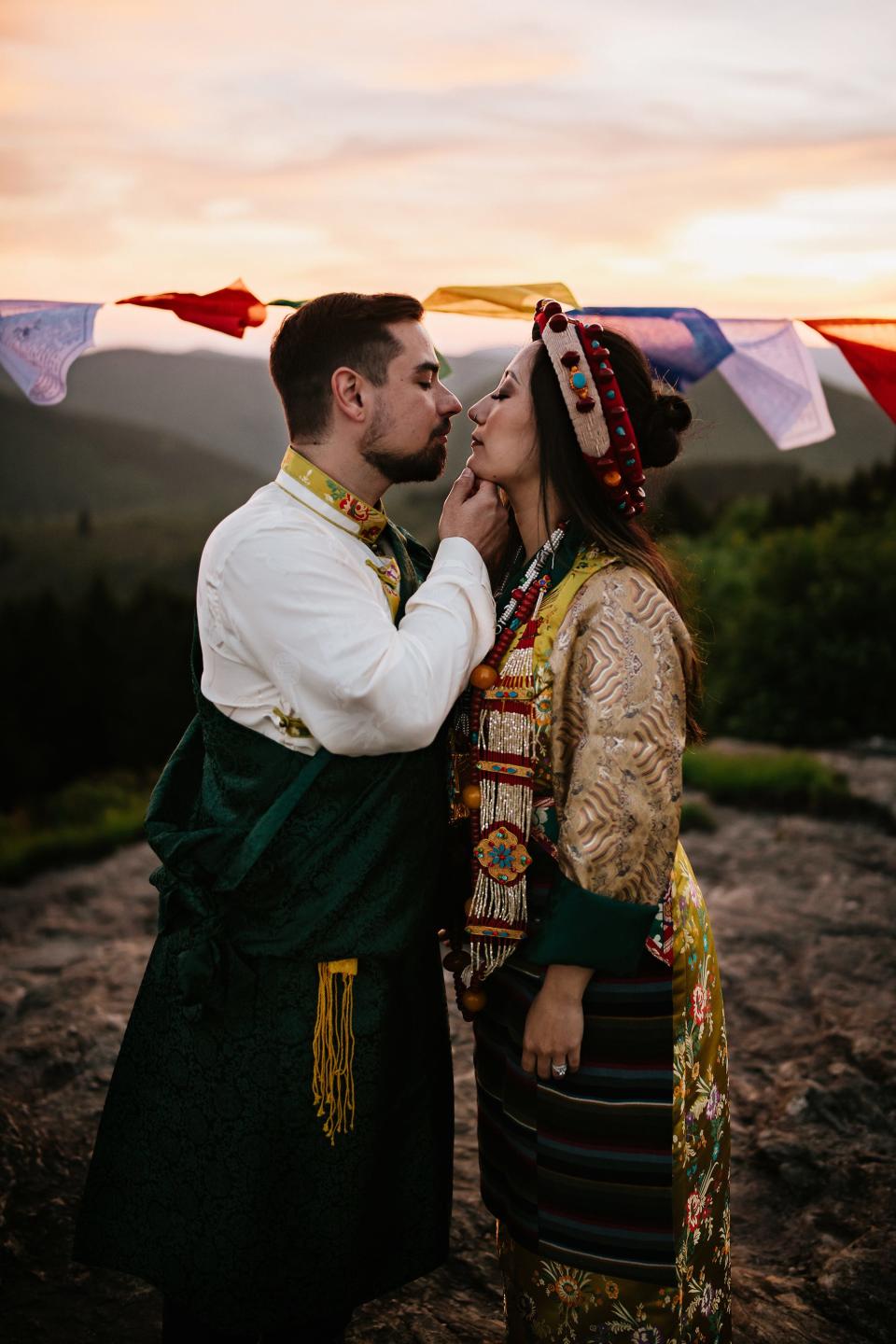 A groom holds his bride's chin on a mountaintop.