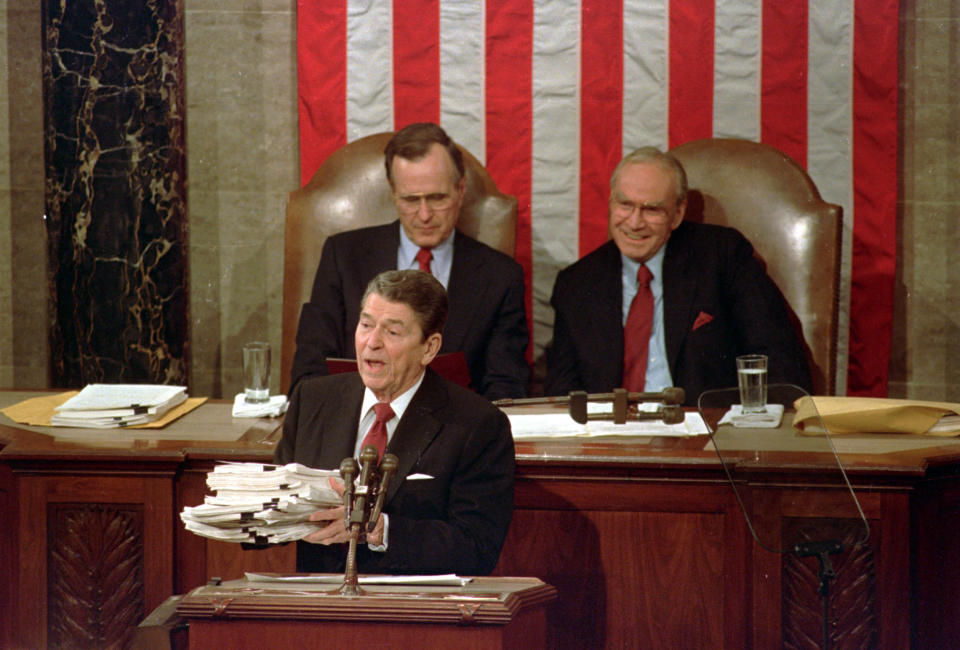 FILE - This Jan. 25, 1988 file photo shows President Ronald Reagan holding up 14-pound continuing resolution for the budget, part of a total package weighing 43-pounds, which the president said was two months late from Congress, during his State of the Union address on Capitol Hill in Washington. Vice President George H.W. Bush, left, and House Speaker James Wright of Texas listen behind him. (AP Photo/Bob Daugherty, File)