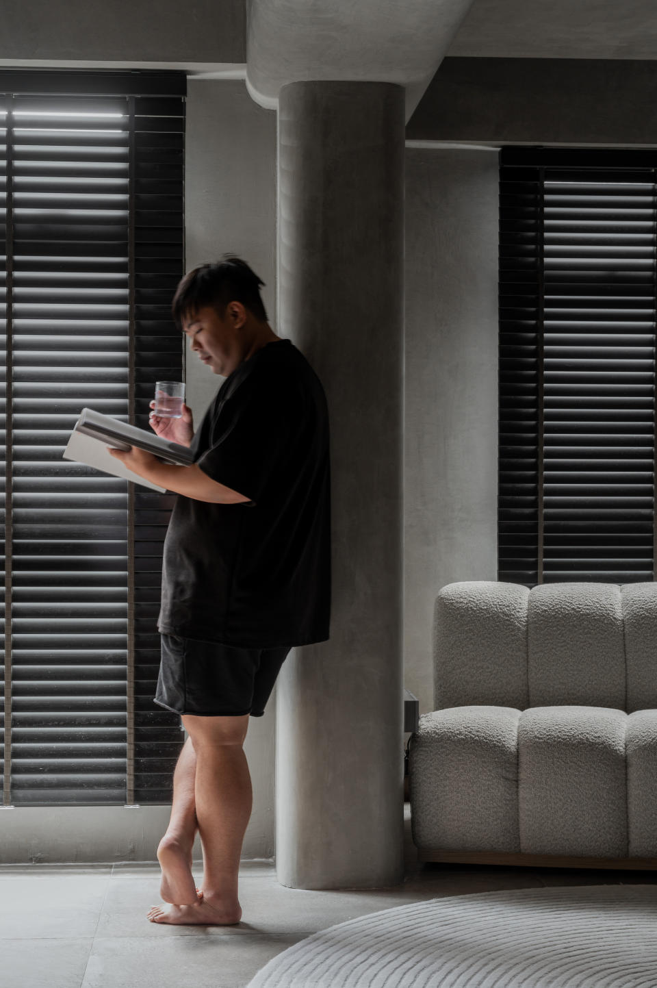 Kelvin Tan, founder of SG Interior KJ and popularly known as comedian Mayiduo, reads his tablet and holds a glass of water while leaning on a column in the living room of his HDB BTO flat.