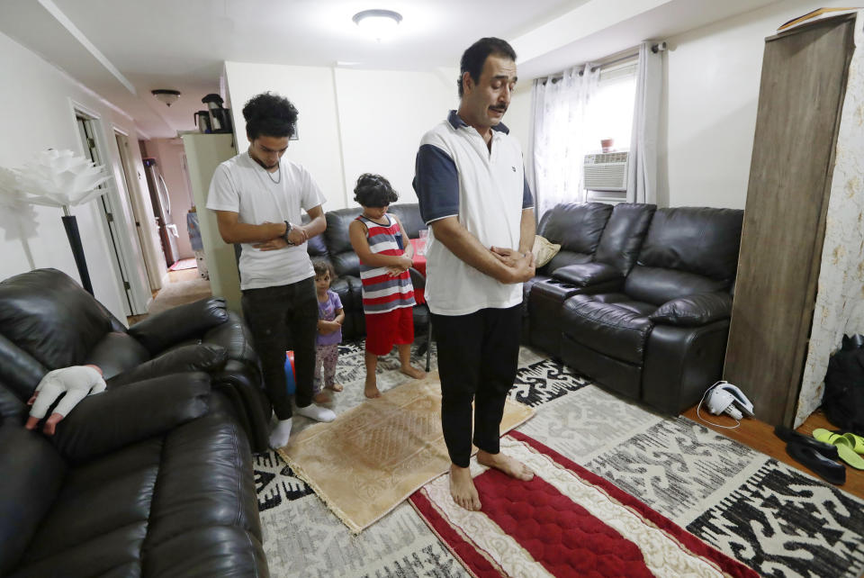 In this Aug. 22, 2019, photo, after arriving home from work, Diaa Alhanoun, right, a Syrian refuge chef, pauses to pray, with his two sons, Nader, 18, left, and Owys, 9, rear, in striped shirt, as Alhanoun's young daugher Masa, imitates the trio, in New York. According to Muslim religious tradition, men and women pray separately, but Masa is too young to understand the concept. (AP Photo/Kathy Willens)