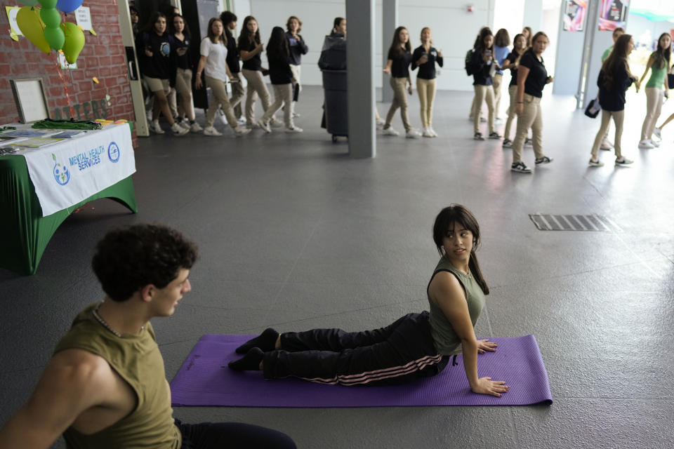 Students leaving lunch watch as Miami Arts Studio junior Alicia Vargas-Romero, 16, practices yoga poses as part of an event to raise awareness about mental health, on World Mental Health Day, Tuesday, Oct. 10, 2023, at Miami Arts Studio, a public 6th-12th grade magnet school, in Miami. (AP Photo/Rebecca Blackwell)